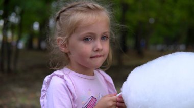 Dışarıda elinde pamuk tutan ve dışarıda yemek yiyen bir kız var.