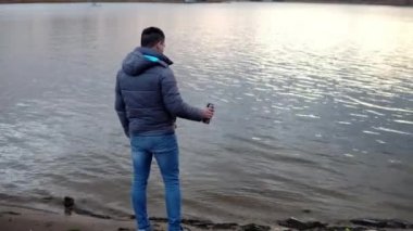 Ceketli bir adam nehrin kıyısında durur, göl ve suya su döker, böylece doğayı kirletir.