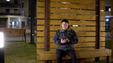 Akşamları yalnız bir adam bankta oturur ve soğuk havada akıllı telefon kullanır.
