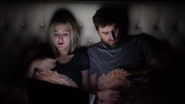 Muž a žena, mladý pár sledování nudný film na notebooku v posteli před spaním — Stock video