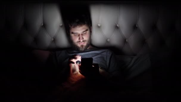 El hombre utiliza el teléfono inteligente en la oscuridad antes de ir a la cama en la cama — Vídeos de Stock