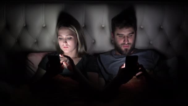 Een man en een vrouw, een jong stel gebruiken een smartphone voordat ze naar bed gaan en elkaar iets laten zien. — Stockvideo