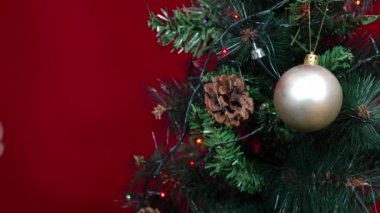 Noel oyuncağı desenli bir top, kırmızı arka planda bir Noel ağacına asılmış.