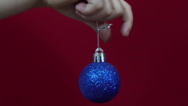Niebieski Boże Narodzenie zabawka w ręku na czerwonym tle zbliżenie — Wideo stockowe