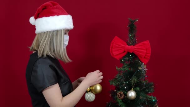 Mujer en sombrero de Santa Claus sobre fondo rojo decora árbol de Navidad — Vídeos de Stock