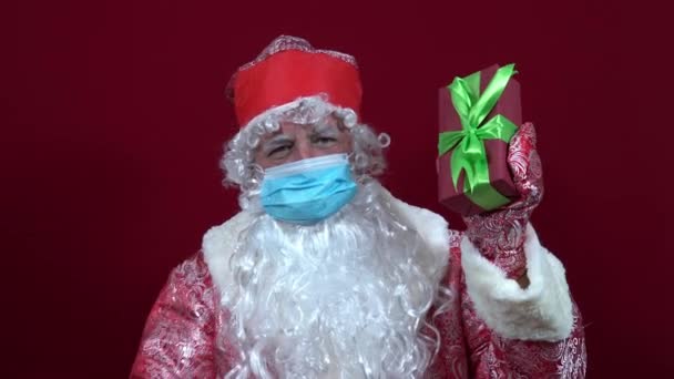 Tıbbi maskeli Rus Noel Baba elinde bir Noel hediyesi tutuyor ve basıyor. — Stok video