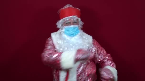 Rus Noel Baba, tıbbi bir maske takmış, neşeli, yaklaşan tatillerden önce kırmızı arka planda dans ediyor. — Stok video