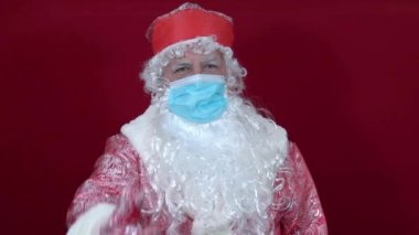 Rus noel baba kırmızı arka planda tıbbi bir maske takıyor.