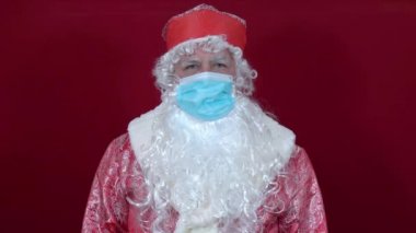 Rus Noel Baba 'nın kırmızı arka plandaki sağlık maskesi iki elinde de onay var.