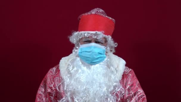 Santa Claus ruso en una máscara médica sobre un fondo rojo se sienta triste sin regalos — Vídeo de stock