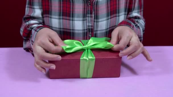 Nő csomagolja karácsony, új év jelen piros csomagolópapír és megfeszíti a zöld szalag íj — Stock videók