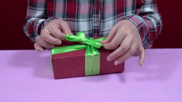 Женщина заворачивает Рождество, новогодний подарок в красную оберточную бумагу и затягивает зеленый бант ленты — стоковое видео