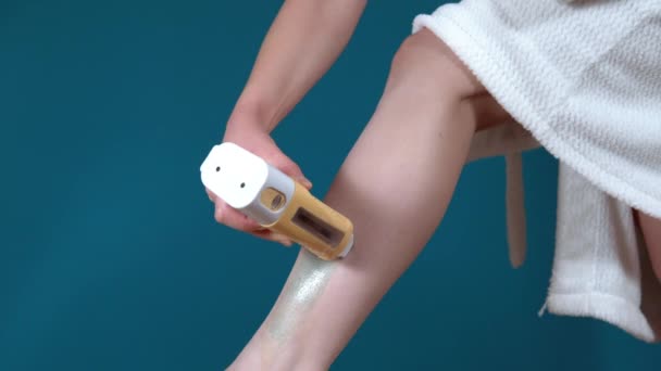 Detailní záběr nohy mladé ženy pomocí voskové epilace doma na tyrkysovém pozadí. Vosk ohřívač pro odstranění chloupků — Stock video