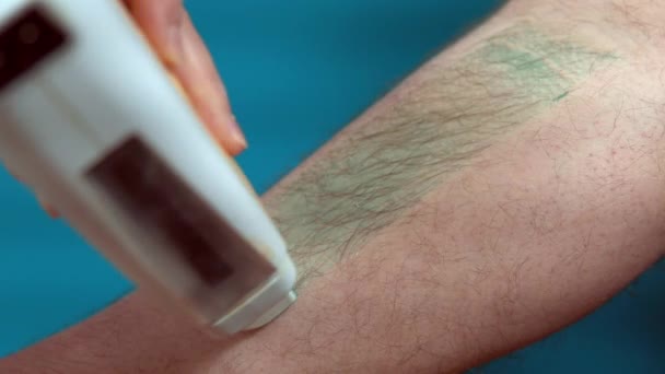 Close-up van harige been van een man met behulp van wax epilatie thuis op een turquoise achtergrond. Body Hair Removal Wax Warmer — Stockvideo
