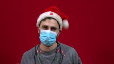 Tıbbi maskeli bir adam kafasında dans eden bir noel şapkasıyla şarkı söyler ve dans eder.