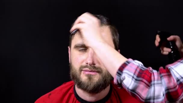 Man kapper sprays spray op zijn hoofd en stijl haar op zwarte achtergrond — Stockvideo