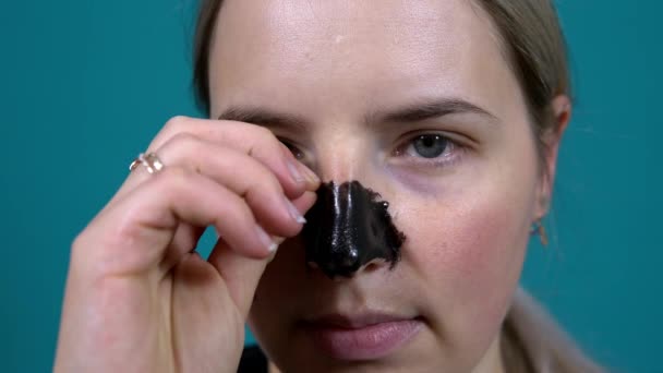 La mujer se quita una máscara negra en la nariz contra puntos negros en la piel — Vídeo de stock