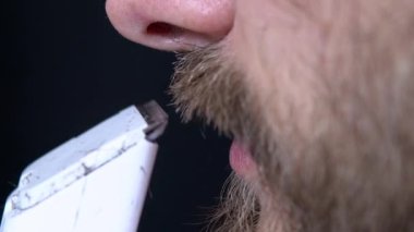 Siyah arka planda tıraş makinesi olan sakallı bir adamın yakın plan fotoğrafı.