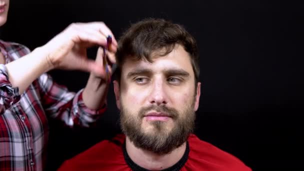 Un hombre en un salón de peluquería una mujer maestra se corta el pelo sobre un fondo negro — Vídeos de Stock