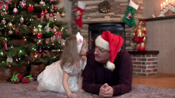 Wnuczka daje dziadkowi prezent świąteczny, całuje i przytula go przy drzewie. — Wideo stockowe