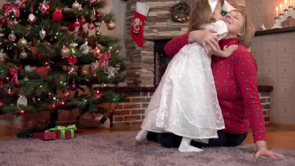 Внучка дарит бабушке рождественский подарок, целует и обнимает её за ёлку. — стоковое видео