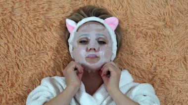 Beyaz cüppeli kadın kozmetik nemlendirici kumaş ve yüz maskesi takıyor.