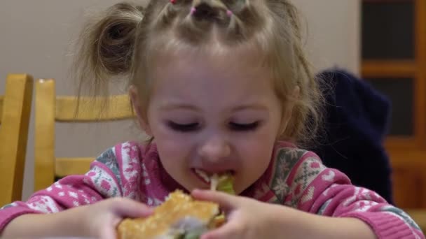 Una ragazzina che mangia hamburger. Bambino a casa con hamburger — Video Stock