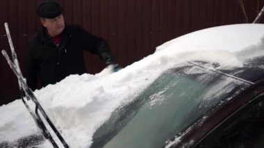 Bir adam bir fırçayla arabanın ön camını kardan temizler. Rusya 'da kış, araba karla kaplıydı.