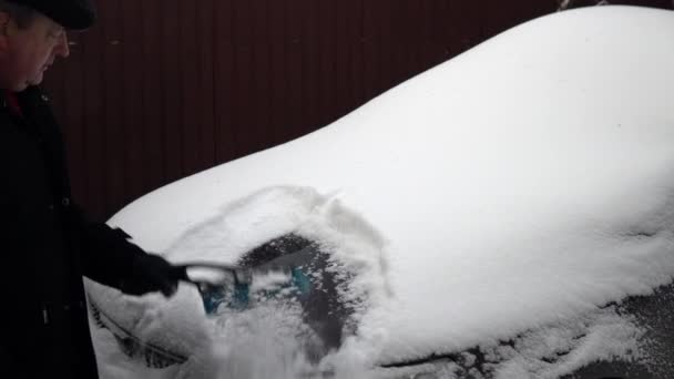 Egy férfi lekeféli a havat a motorháztetőről. Oroszországban a telet hó borította. — Stock videók
