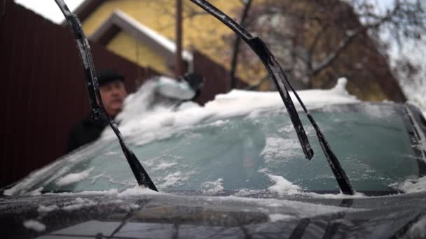 Een man reinigt een voorruit van sneeuw met een borstel. Winter in Rusland, de auto was bedekt met sneeuw — Stockvideo