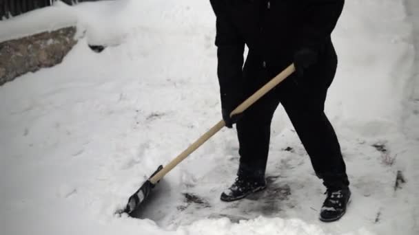 Ένας άντρας με μαύρα ρούχα καθαρίζει το χιόνι με ένα φτυάρι στην αυλή του. Χειμώνας στη Ρωσία κάλυψε την αυλή με χιόνι — Αρχείο Βίντεο