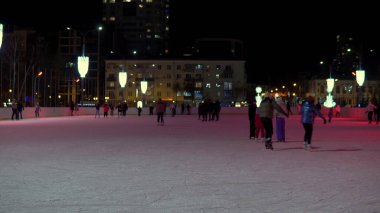 İnsanlar buz pateni pistinde kayıyorlar. Rusya 'da kış, akşam saatlerinde insanlar buz pistinde.