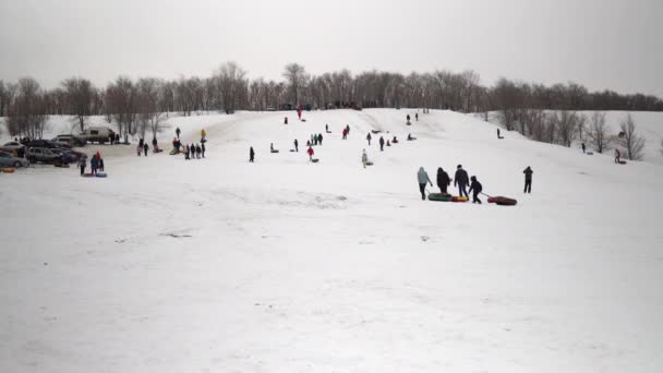 Bir grup insan kar kayaklarına biniyor. Çocuklar kendilerini şişme halkalardaki buz kaydırağında listeler. Kızaklar, plastik buz pateni pistleri — Stok video