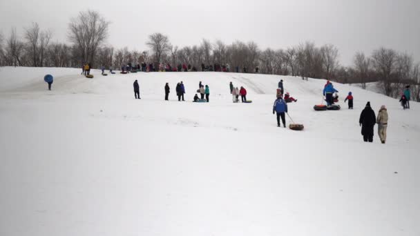 Une foule de gens roulent sur des glissades de neige. Les enfants se listent sur la glissière de glace sur des anneaux gonflables. traîneaux, patinoires en plastique — Video