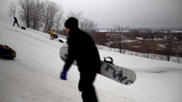 Une foule de gens roulent sur des glissades de neige. Les enfants se listent sur la glissière de glace sur des anneaux gonflables. traîneaux, patinoires en plastique — Video