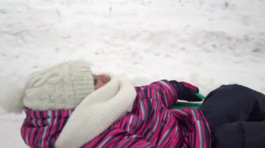 Kız karda şişme bir yüzükle yuvarlanıyor. Kalın elbiseli bir kız şişme bir yüzükte yatıyor ve başka biri tarafından bir iple çekiliyor.