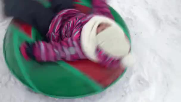 La chica está siendo girada en un anillo inflable en la nieve. Una chica en ropa de abrigo se encuentra en un anillo inflable y se desenrolla con una cuerda — Vídeos de Stock