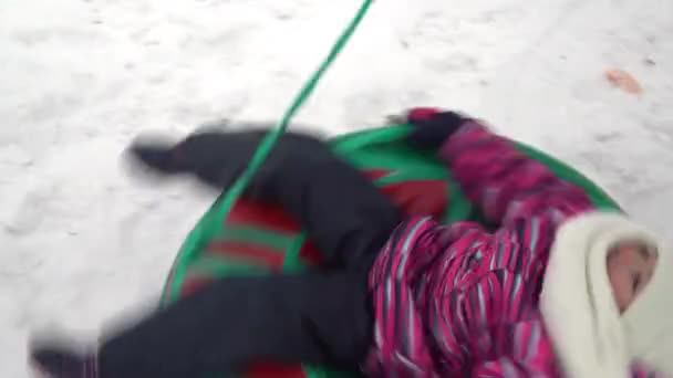 Das Mädchen wird auf einem aufblasbaren Ring im Schnee gesponnen. Ein Mädchen in warmer Kleidung liegt auf einem aufblasbaren Ring und wird mit einem Seil abgewickelt — Stockvideo