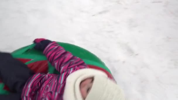Jenta blir spunnet på en oppblåsbar ring i snøen. En jente i varme klær ligger på en oppblåsbar ring og er løs med et tau. – stockvideo