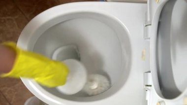 Lastik eldivenli bir ev hanımı klozeti özel bir temizleyici ve fırçayla temizler.