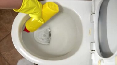 Lastik eldivenli bir ev hanımı klozeti özel bir temizleyici ve fırçayla temizler.