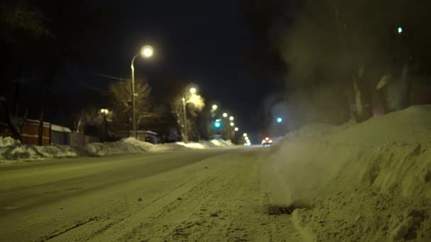 Rosyjska zimowa droga wieczorem. Para wypływa z kratki ściekowej na drodze. — Wideo stockowe