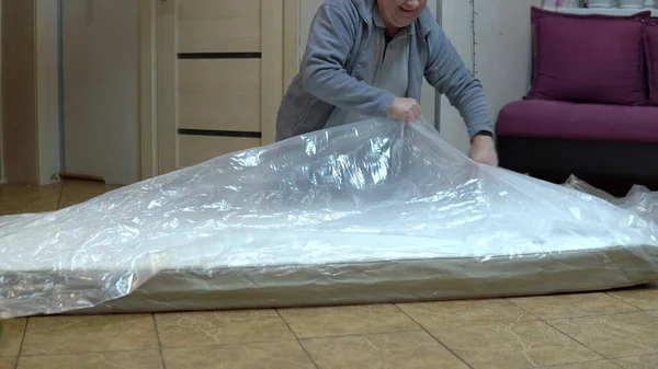 Ein erwachsener Mann packt eine neue Matratze aus. Auspacken der Matratze mit einem in die Tasche gepressten Messer — Stockfoto