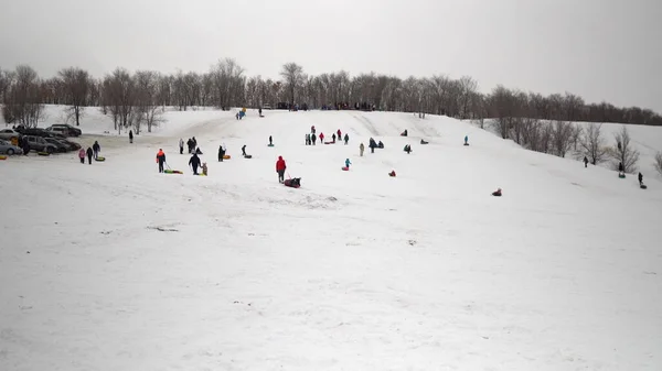Bir grup insan kar kayaklarına biniyor. Çocuklar kendilerini şişme halkalardaki buz kaydırağında listeler. Kızaklar, plastik buz pateni pistleri — Stok fotoğraf