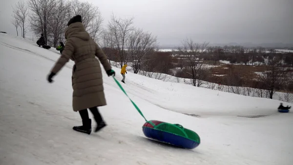 Een menigte van mensen rijden op sneeuw glijbanen. Kinderen zetten zichzelf op de ijsglijbaan op opblaasbare ringen. sleeën, kunststofschaatsbanen — Stockfoto