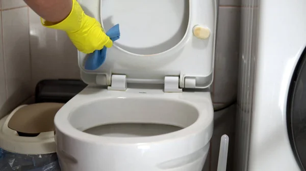 Eine Hausfrau in Gummihandschuhen reinigt die Toilettenschüssel mit einem Spezialreiniger und einer Bürste — Stockfoto