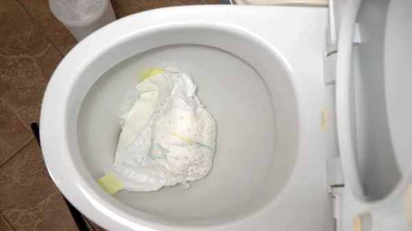 Großaufnahme, wie man eine schmutzige Babywindel in die Toilette wirft. Es verstopft die Toilettenspülung — Stockfoto