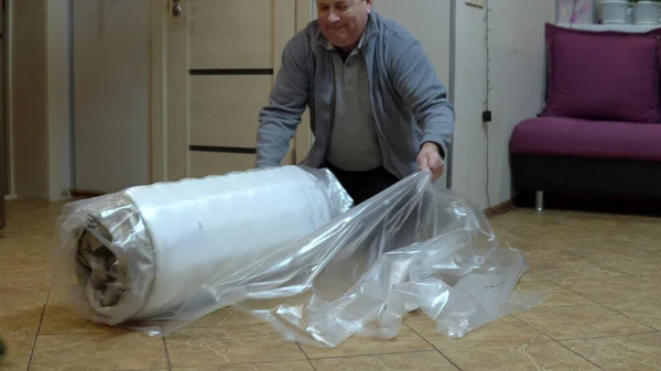 A grown man unpacks a new mattress. Unpacking the mattress with a knife pressed into the bag Stock Picture