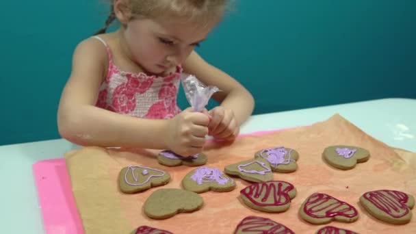 Het meisje versiert koekjes in de vorm van een hart met zoete roze glazuur. koekjes bakken voor Valentijnsdag — Stockvideo