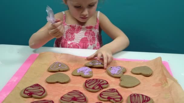 Pigen dekorerer cookies i form af et hjerte med sød lyserød glasur. Gøre cookies til Valentinsdag – Stock-video